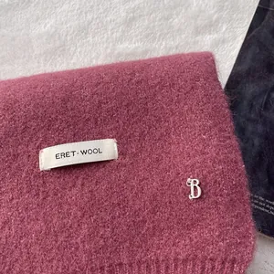 Close-up of pink knit wool scarf featuring an ERET WOOL label and silver B charm detail
