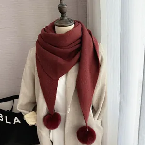 Détail d'une écharpe en tricot bordeaux avec de gros pompons doux en fausse fourrure