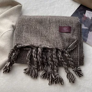 Détail d'une écharpe à carreaux avec franges torsadées et étiquette de marque textile