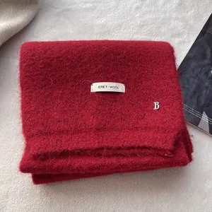 Detail of red wool knit scarf featuring a white woven label and silver metal B pendant