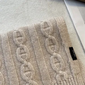 Close-up of 100% pure wool scarf showing beige chunky knit chain pattern and label