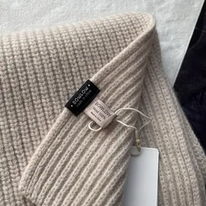 Nahaufnahme des BOWLOW-Etiketts mit 100% Wolle auf beigem geripptem Strickgewebe