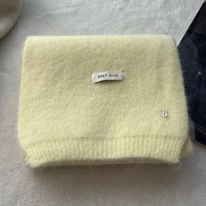Close-up of soft yellow wool knit scarf featuring a silver metal B pendant detail