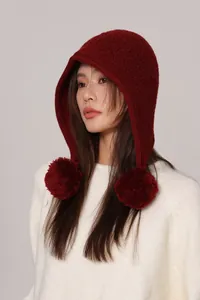 Dettaglio del passamontagna in lana rosso scuro con grandi pompon e maglia testurizzata