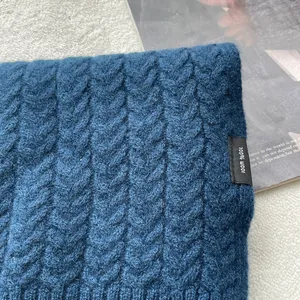 Dettaglio di sciarpa in lana blu navy con trama a trecce ed etichetta 100% lana
