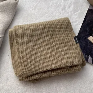 Detail eines kamelfarbenen Wollschals mit 100% Wolle-Etikett und Rippenstrick-Struktur