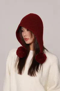 Dettaglio del passamontagna in maglia con pompon soffici in rosso scuro, texture morbida