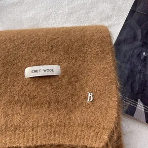 Close-up of caramel wool knit scarf with brand label and silver metal B ornament