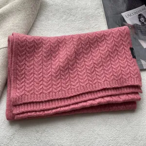 Dettaglio di sciarpa in lana rosa con trama a trecce ed etichetta 100% lana