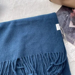 Detailed close-up of dark blue 100% pure wool scarf with tassel fringe and quality tag