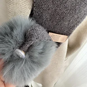 Détail d'une écharpe en maille grise avec pompon en fausse fourrure et bouton transparent