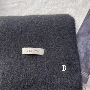 Detail of black wool scarf featuring ERET label and silver metal B logo accessory