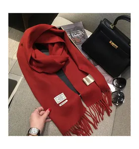 Dettaglio di sciarpa rossa in 100% lana con frange accanto ad accessori moda