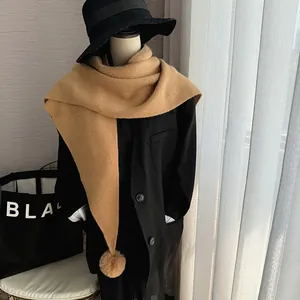 Gros plan sur une écharpe triangle en tricot camel avec un pompon en fausse fourrure