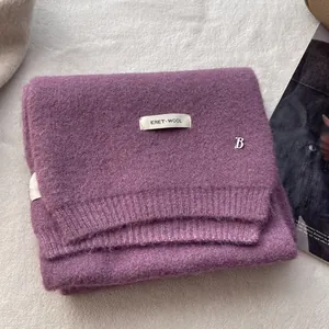 Detail of purple wool scarf with a white ERET WOOL label and silver B initial metal tag