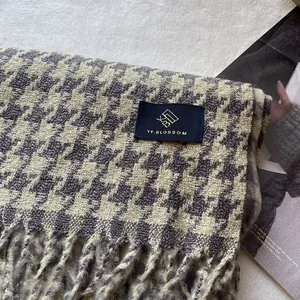 Detailaufnahme des dicken grau-cremefarbenen Hahnentritt-Schals mit Logo-Label und Quasten