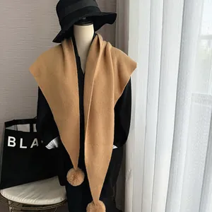 Vue détaillée d'une écharpe en tricot camel avec pompons en fourrure et tissage épais