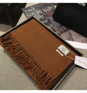 Dettaglio di sciarpa di lana color caramello con nappe in una scatola regalo nera