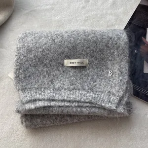 Detailed texture of grey wool knit scarf featuring a silver metal letter B logo