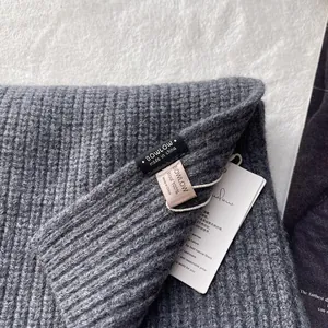Detailaufnahme der 100% Woll-Rippstrickstruktur und Markenetiketten am grauen Schal