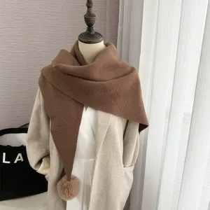 Détail d'une écharpe triangulaire en maille marron foncé avec pompon sur manteau beige