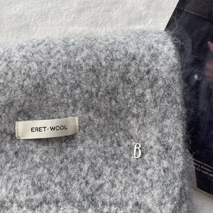 Close-up of grey wool knit scarf with brand label and silver metal B logo detail