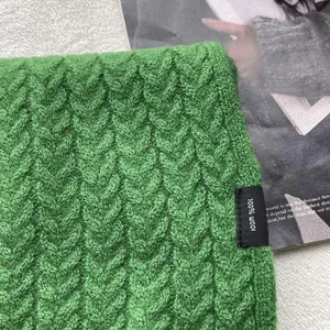 Dettaglio ravvicinato della sciarpa in maglia a trecce verde con etichetta 100% pura lana