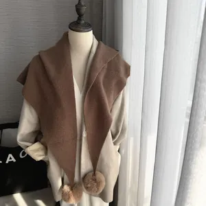 Détail d'une écharpe en maille marron avec des pompons doux en fausse fourrure peluche