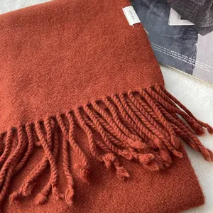 Close-up of burnt orange wool scarf featuring 100% wool label and woven fringe detail