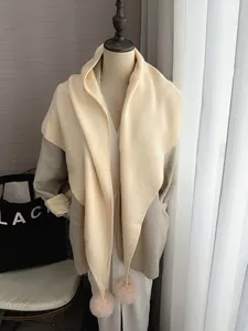 Détail d'une écharpe en maille douce avec pompons en peluche et design bicolore chic