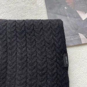 Dettaglio dell'etichetta 100% lana su sciarpa in maglia a trecce nera con trama spessa