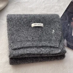 Close-up of dark grey wool knit scarf with brand label and silver metal B pendant
