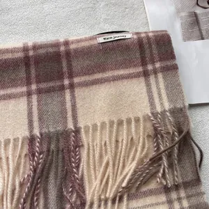Detailopname van de franjes en textuur van de wollen ruitjes sjaal met merklabel