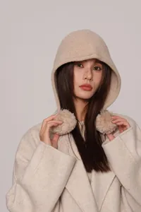 Dettaglio del passamontagna in lana beige con pompon indossato da una modella in cappotto