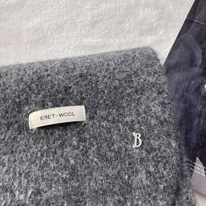 Close-up of dark grey wool scarf featuring a white brand label and silver metal B logo