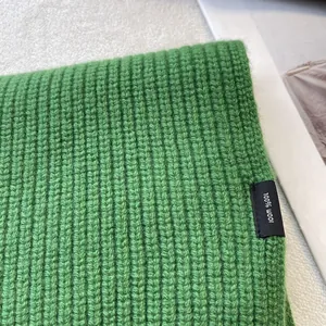 Detailansicht des grünen Wollschals aus 100% Wolle mit grober Rippstrick-Textur und Etikett