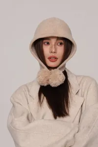 Dettaglio del passamontagna in lana beige con grandi pompon e morbida trama a maglia