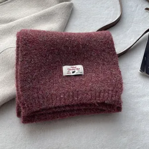 Detailed texture of burgundy wool blend scarf with a vintage knitted finish and white label