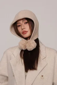 Dettaglio passamontagna in lana beige con due grandi pompon e morbida trama in maglia