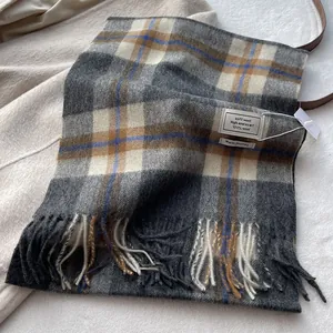 Macro detail of the 100% wool scarf showing woven plaid texture and fringed edges