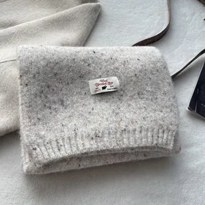 Close-up of wool blend knit scarf in oatmeal with colorful Donegal texture and woven label