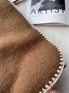 Detailed close-up of brown wool scarf with white blanket stitch edges and soft texture