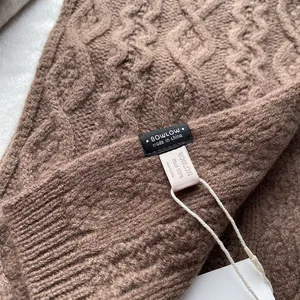 Detailed macro view of 100% Merino wool label on thick brown cable knit winter scarf