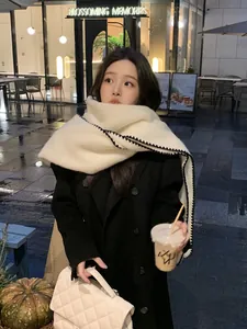 Detail of off-white thick wool scarf with black scalloped edge on model in winter coat