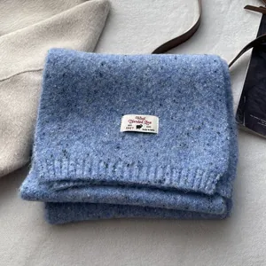 Detail of wool blend knitted scarf in sea salt blue with speckled texture and brand label