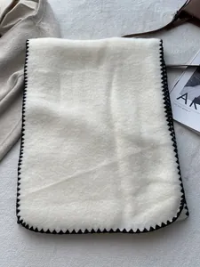 Detail of soft cream wool scarf with contrast black stitched edges and warm texture