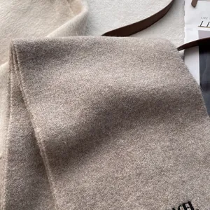 Detailed macro shot of the oatmeal knitted scarf with elegant black embroidered letters