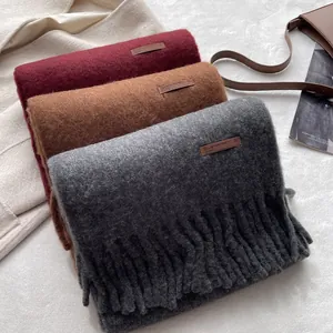 Detail of wool-like scarves in wine red, tan, and dark grey with fringe and leather tags