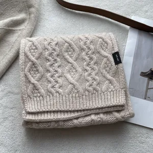 Close-up of cable knit texture on 100% merino wool scarf with premium woven brand label