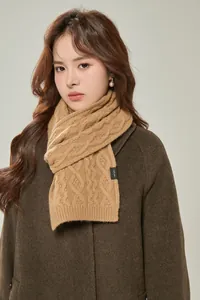Close-up of cable-knit camel wool scarf featuring 100% wool material label and thick texture